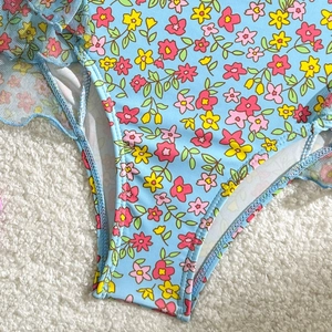 Détail d'un bikini bleu clair à fleurs avec imprimés jaunes et volants en tulle latéraux