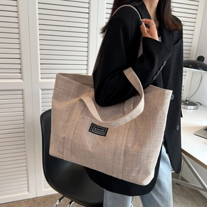Minimalist beige canvas tote bag with black Fashion label shown on model in black suit