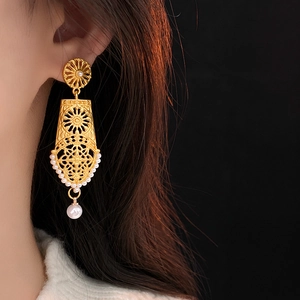 Close-up of vintage hollow flower pearl drop earrings worn by a model in soft lighting