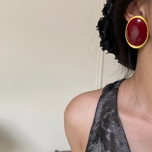 Close-up of retro oval earring with deep red finish and thick matte gold frame on model