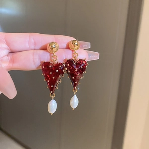 Détail de la boucle d'oreille cœur rouge avec clous dorés et pendentif perle blanche