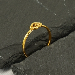 Dettaglio dell'anello regolabile in acciaio dorato con nodo a spirale su pietra grigia