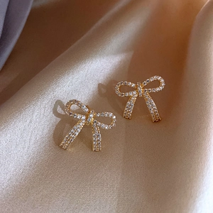 Macro shot of gold bow knot earrings featuring white zircon pavé on champagne silk