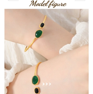 Close-up of golden open bangle with green and black oval gemstones on model's wrist