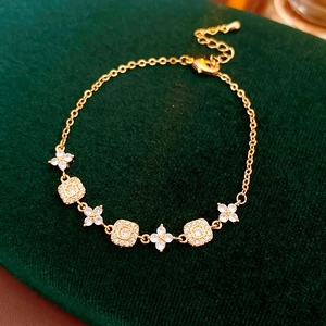 Close-up of gold-plated bracelet with flower and square charms on green velvet