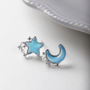 Close-up of asymmetric star and moon earrings with blue stones and pearls on white surface