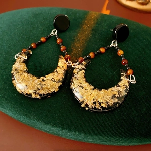 Macro detail of crescent resin earrings with gold foil on a green velvet cushion