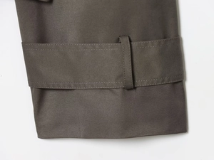 Close-up of the dark taupe twill fabric stitching and cuff strap detail on the trench coat