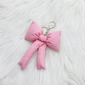 Detailed close-up of a pink fabric bow keychain with silver metal clasp on white faux fur