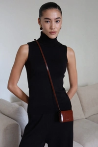 Detailed shot of black sleeveless high neck knitwear paired with a brown leather mini bag