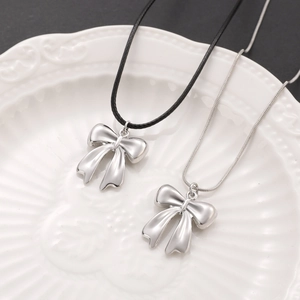 Detailed view of elegant silver bow pendants with black cord and metal chain on ceramic tray