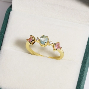 Detailed close-up of a golden flower ring with light blue oval stone and pink gems