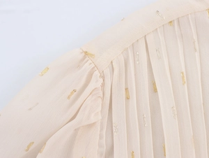 Macro shot of pleated shoulder detail on beige chiffon dress with metallic gold threading