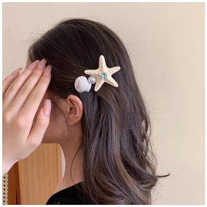 Close-up of starfish and seashell hair clip with pearls on brown wavy hair