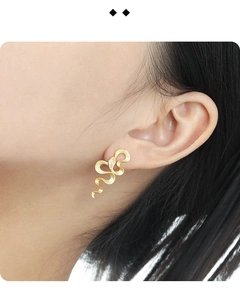 Close-up of snake texture gold earring with zircon studs worn on female model ear