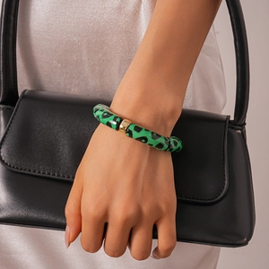 Detail of green and black leopard print acrylic bracelet with a gold metal clasp on wrist