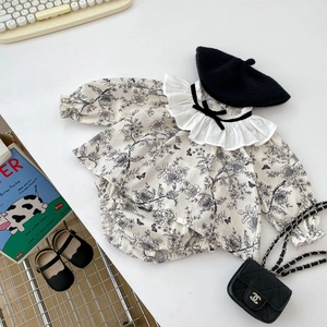 Detail of floral baby top with lace collar and black ribbon bow on white tabletop