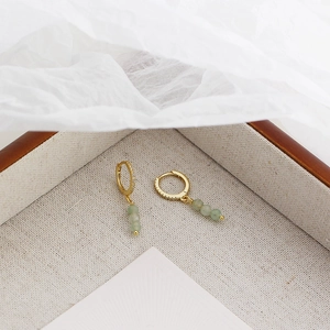 Macro detail of gold hoop earrings with small crystals and hanging green aventurine beads