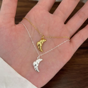 Detail of gold and silver croissant pendant necklaces held by hand over a wooden base