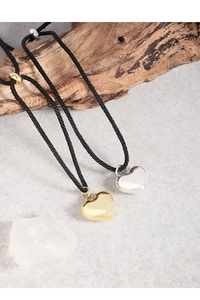 Detail of silver and gold heart pendants on black adjustable cords against wood and stone