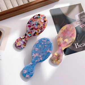 Three acetate hair combs with colorful terrazzo patterns on a stylish wooden tray display