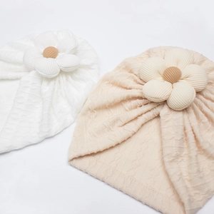 Detail of soft waffle knit texture and 3D flower on baby turban caps in white and beige