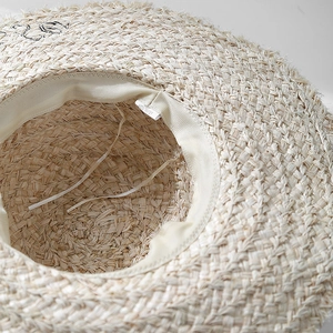 Close-up of raffia sun hat showing 100% paper material label and woven texture details