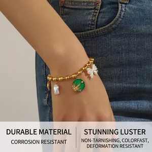 Detail of gold beaded bracelet with baroque pearl, resin bow, and green enamel sun charm