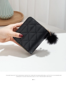 Close-up of black quilted small wallet with golden zipper and fluffy pompom keychain