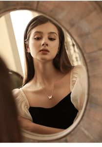 Elegant gold butterfly necklace and earring set shown reflected in a vintage round mirror