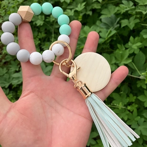 Detailed view of mint green silicone bead keychain with wood charms held in hand