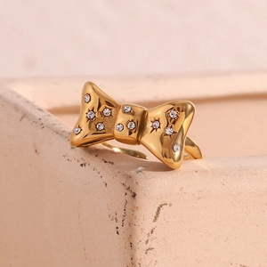 Detail of 18K gold plated bow ring with micro-set sparkling crystals on a stone surface