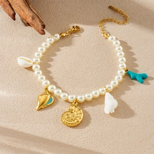 Bracelet de perles fantaisie avec pendentifs de conque dorée et corail sur fond de sable