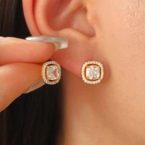 Elegantes pendientes de botón cuadrados dorados con halo de circonitas puestos en el lóbulo