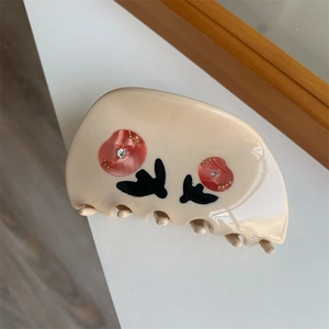 Close-up of beige hair claw clip featuring red floral patterns with sparkling rhinestones