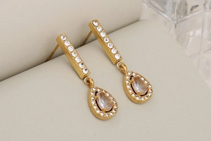 Dettaglio di orecchini pendenti placcati oro con strass rettangolari e a forma di pera
