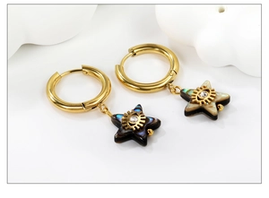 Close-up of golden hoop earrings with abalone star charms and crystal eye detail