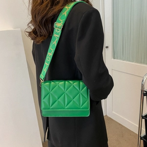 Detail of green quilted crossbody bag with a wide patterned strap and gold hardware