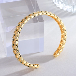 Detail of 18k gold open cuff bracelet featuring green gemstones and hollow lattice mesh