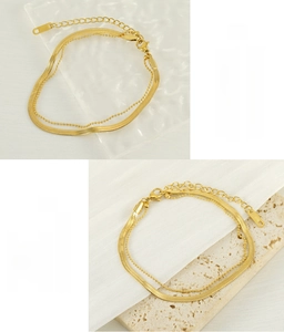 Detail of 18K gold plated flat snake chain and beaded anklet set on stone surface