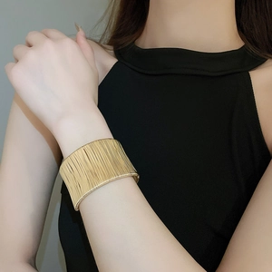 Close-up of a wide gold metal cuff bracelet with fine vertical textured finish on a model