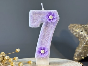 Close-up of a purple number 7 birthday candle with glitter finish and floral decor