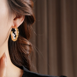 Detail of C-shaped gold-plated earrings with pearls on model in close-up view