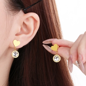 Detailed close-up of golden heart-shaped earrings with round clear crystal drops on model