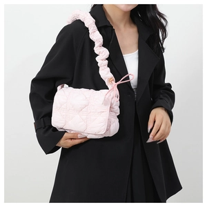 Detail of light pink quilted nylon bag featuring a puffy cloud strap and ribbon bow