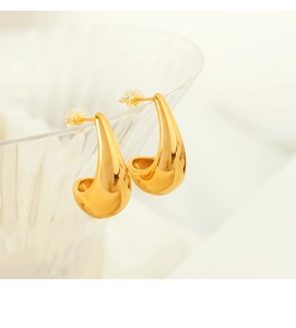 Detailed close-up of golden teardrop earrings on a glass rim with high polish finish