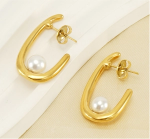 Macro detail of U-shaped gold earrings with white pearls on a minimalist stand