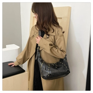 Dettaglio della borsa hobo nera con borchie dorate indossata su un trench marrone