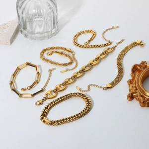 Detailed close-up of 18K gold-plated Cuban and snake chain bracelet sets on white stone