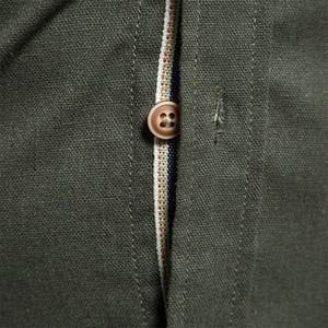 Détail d'une chemise en coton vert armée avec tissu texturé, bouton brun et liseré